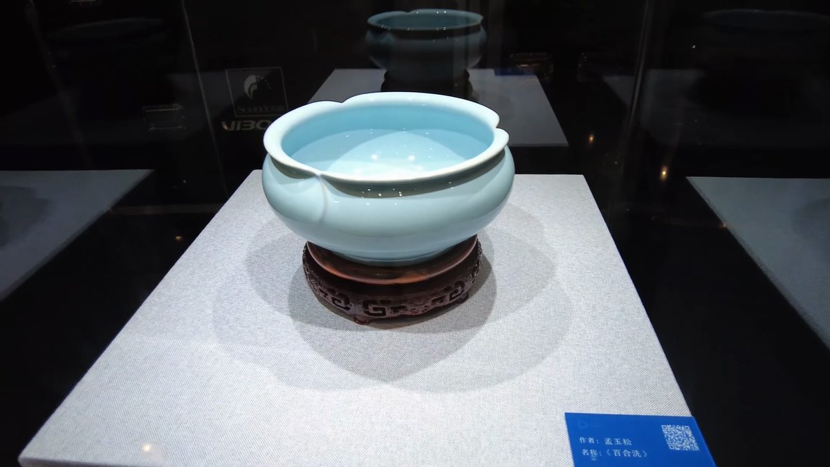 A pale celadon-glazed bowl on a carved wooden