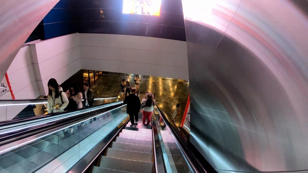 A second escalator descending past a curved pink