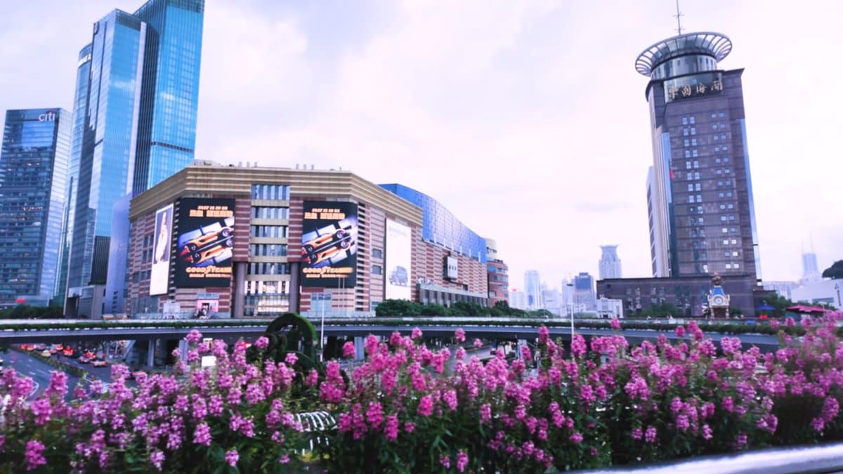 A shopping mall facade with large screens, flowerbeds