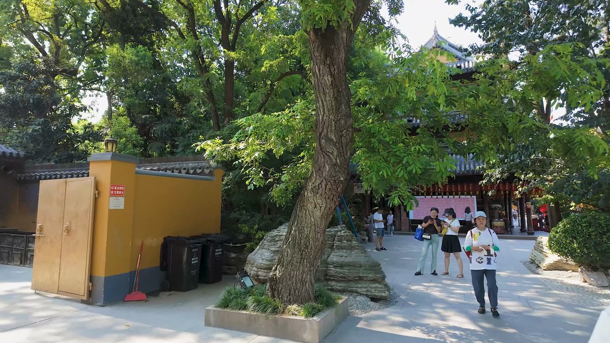 A yellow-walled kiosk beneath a tree, visitors walking